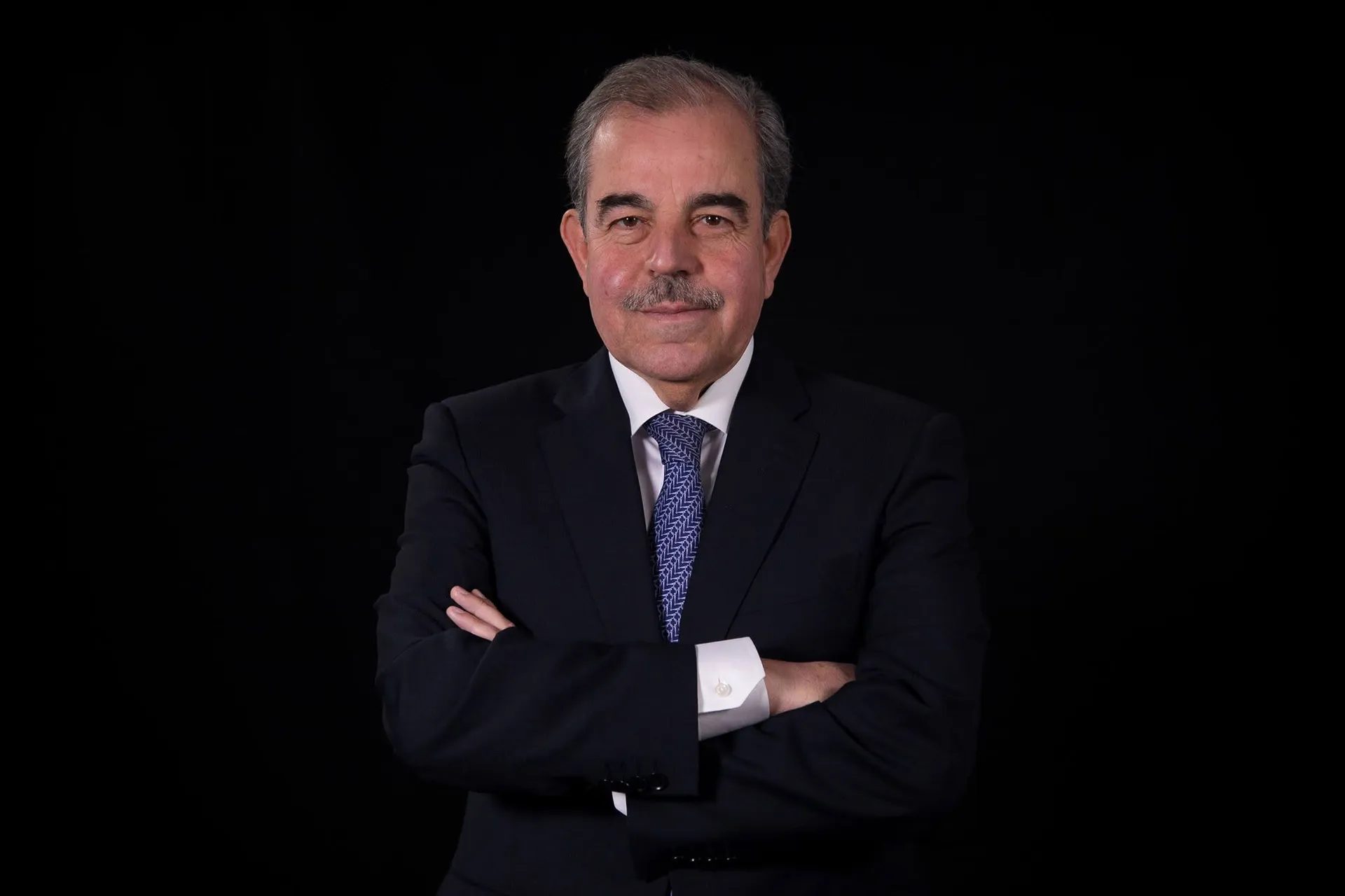 Portrait de Mondher Zenaidi en costume sombre, bras croisés, sur fond noir